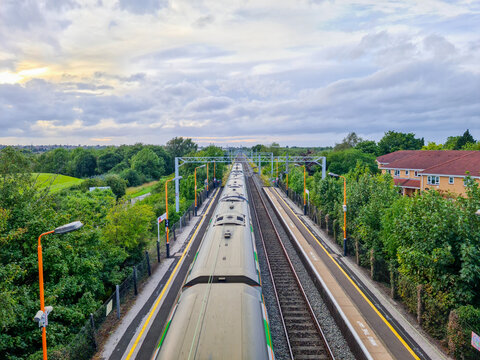 View of Marston Green Station with a train at the platform, surrounded by trees and residential buildings under a cloudy sky in Marston Green, England, United Kingdom.