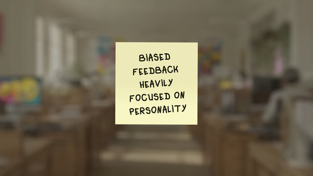 Sticky memo with the words "biased feedback heavily focused on personality" in the close-up, superimposed on a blurred background showing an cubicle-free environment.