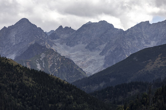 View of Rusinowa Polana with the rugged peaks of the Tatra Mountains rising above dense coniferous forests under a cloudy sky in Tatra County, Lesser Poland, Poland.