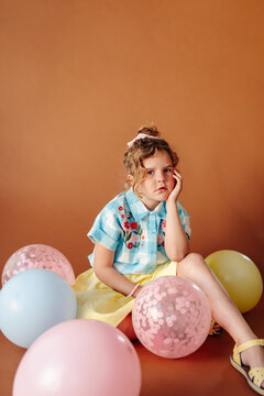 Serious girl sitting amongst colorful balloons