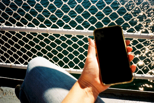 POV view of woman holding mobile phone while traveling on ferry boat