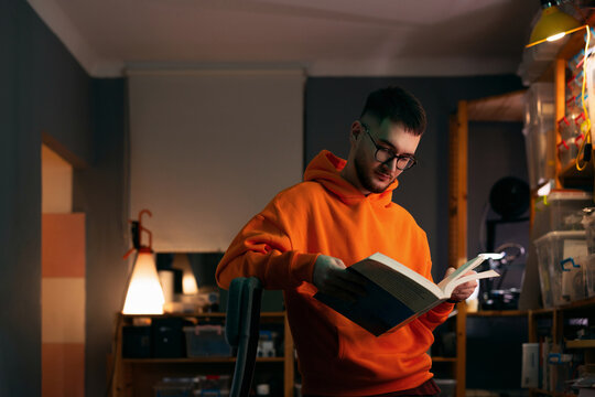 Young Man Reading a Book in Orange Hoodie Indoors