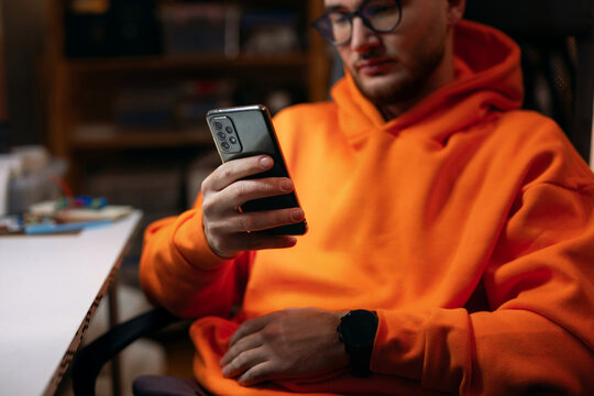 Young Man in Orange Hoodie Using Smartphone at Desk
