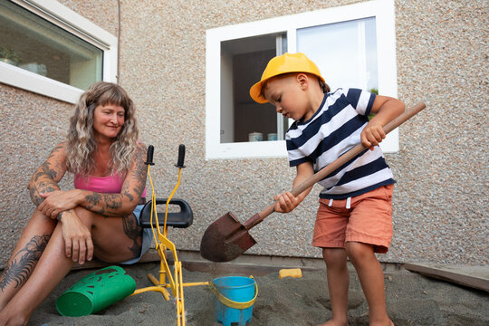 Mother watching son dig in sandbox while wearing toy hard hat