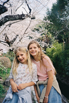 Two young blonde girls smiling together beneath cherry blossom