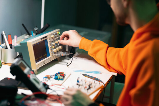 Electronics Engineer Testing Circuit with Oscilloscope at Workbench