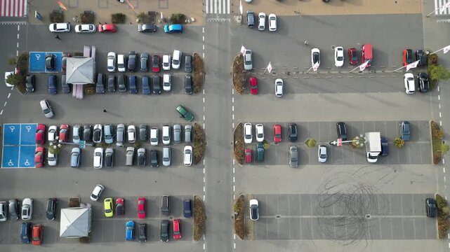 Aerial view of busy parking lot near shopping center, showcasing various vehicles in organized rows, with gradual camera zoom out revealing scene dynamics and spatial arrangement