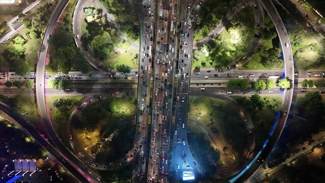 Aerial view of the Semanggi Interchange at night with heavy traffic flowing through the cloverleaf junction surrounded by illuminated city greenery in Jakarta Selatan, DKI Jakarta, Indonesia.