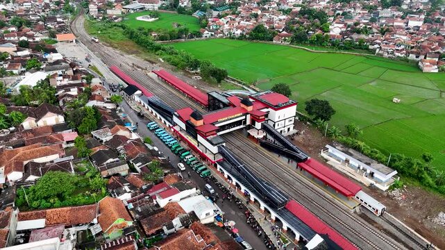 Bandung, West Java, Indonesia - 12 May 2025: Aerial view of Cicalengka Railway Station with its red roof platforms, surrounding residential houses, and adjacent green rice fields.