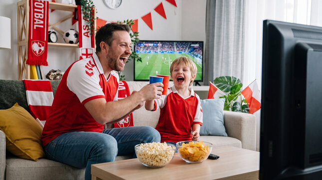 A father and son clink drinks while watching football, capturing excited Big Game Day family moments for indoor campaign posters.