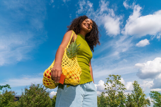 Young woman carrying reusable fruit bag under blue sky