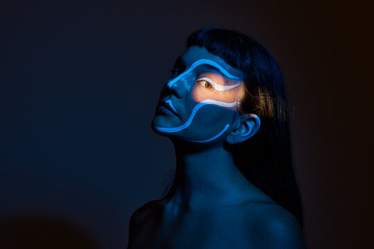 Woman with blue and white face paint posed in low light