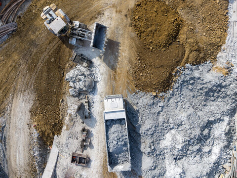 Aerial view of a construction site featuring a yellow wheel loader and a dump truck parked on a dirt ground with piles of gravel and earth in Istanbul, Istanbul, Turkiye.