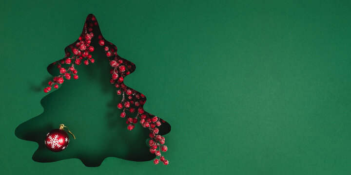 Creative Christmas banner featuring a paper cut fir tree silhouette over dark background, adorned with red bauble and decorative winter berries. Elegant New Year greeting card with large copy space.
