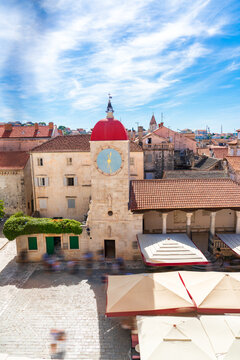 Elevated vertical view of the historic center of Trogir, showing the town&rsquo;s distinctive red-tiled roofs, stone buildings, clock tower and busy square with cafe terraces