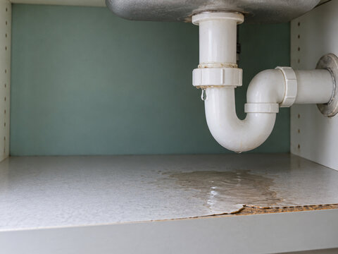 Leaking white plastic sink drain pipe causing water damage in cabinet