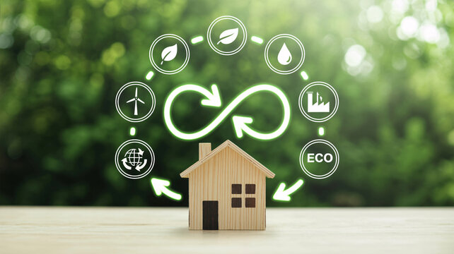 Small wooden model house sitting on surface beneath glowing circular ecology icons representing sustainable living renewable energy green technology recycling concepts and environmental protection ini