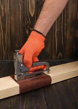 A craftsman fixing an abrasive sanding sheet onto a timber block using a professional construction stapler. Handyman process of making a DIY hand sander in a home workshop.