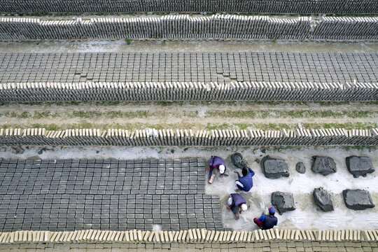Aerial view of workers stacking and arranging rows of clay bricks in a large brickyard in Dhaka, Dhaka Division, Bangladesh.