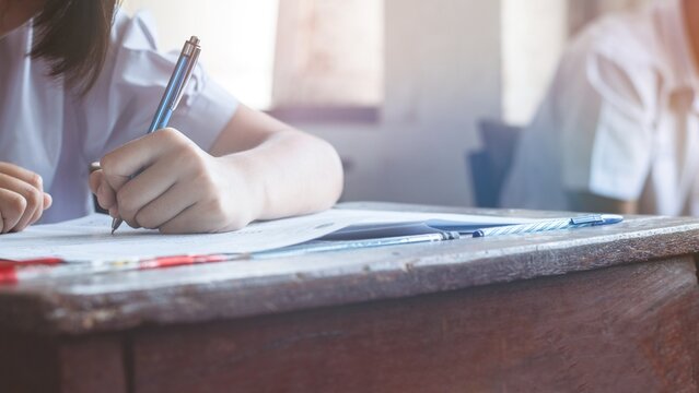 Close-up of Asian Female Student Hand Writing Exam Paper on Desk in Classroom