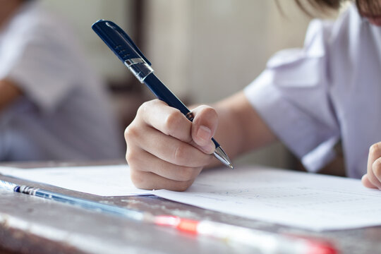 Extreme Close-up of Student Hand Holding Blue Pen Writing Exam Paper on Desk