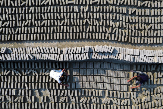 Aerial view of a brickyard with rows of drying mud bricks and two workers arranging them in Gaibandha Sadar Upazila, Rangpur Division, Bangladesh.