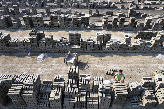 Aerial view of a brickyard with rows of stacked clay bricks, a worker arranging bricks, and a wheelbarrow in Gaibandha Sadar Upazila, Rangpur Division, Bangladesh.