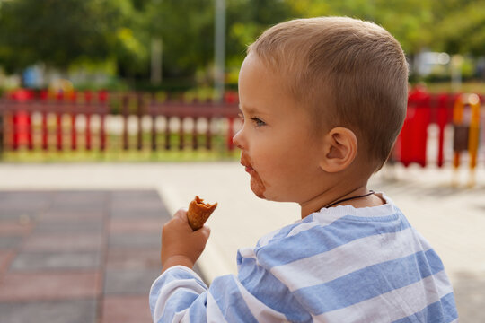 Side view profile of a little toddler boy eating an ice cream waffle cone outdoors at a park.