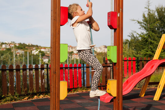 Side view of a little girl climbing up a rope on an outdoor playground structure.