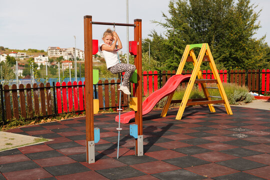 Little girl climbing up a climbing rope on an outdoor playground with a colorful slide.