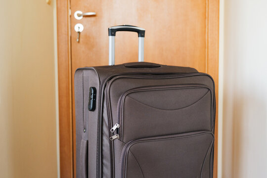 Close-up of a brown travel suitcase with an extended handle standing in a hallway near a closed wooden door.