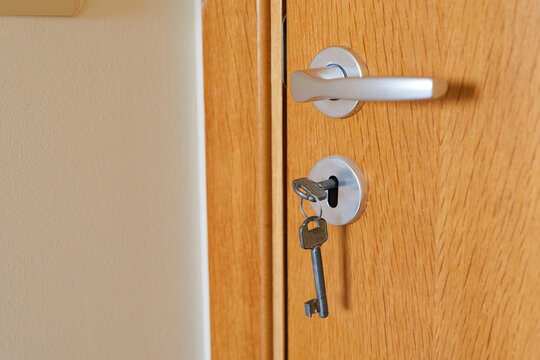 Close-up of metal keys inserted in the lock of a closed light wooden door in an apartment or hotel room.