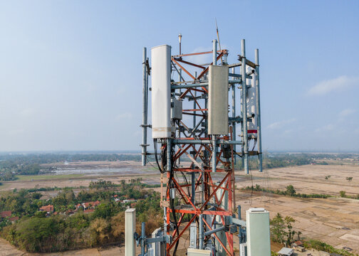 Aerial view of a telecommunications tower with antennas rising above rural fields and trees in Central Java, Indonesia.