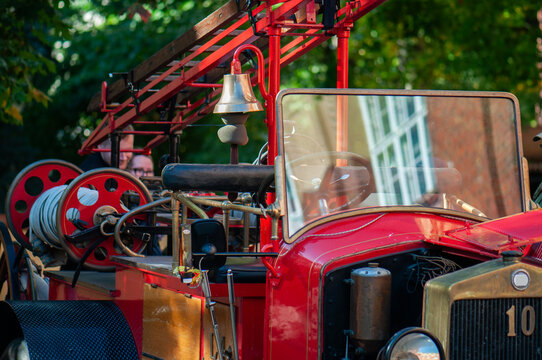 Vintage red fire engine displayed in a fire station courtyard, featuring classic metal bodywork, large headlights, hose reels and traditional firefighting equipment.