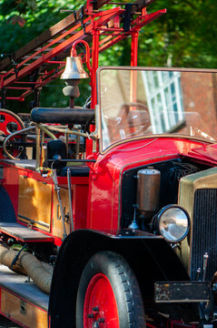 Vintage red fire engine displayed in a fire station courtyard, featuring classic metal bodywork, large headlights, hose reels and traditional firefighting equipment.