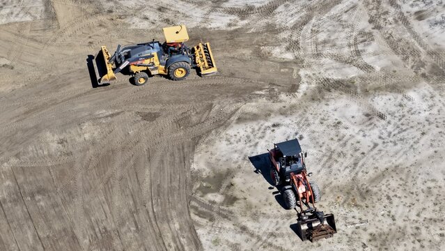 Aerial view of a yellow tractor and a red tractor working on a dirt construction site in World Golf Village, Florida, United States.