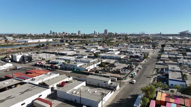 Long Beach, California, USA - Low Drone View of Westside Industrial Warehouses and Factories With Downtown Skyline in the Distance on a Bright Day