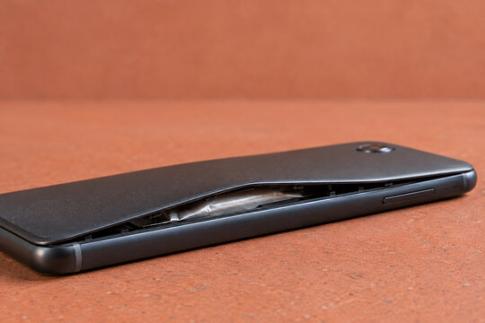 Swollen smartphone battery lifting black phone cover on orange surface