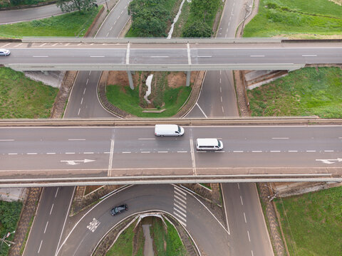 Aerial view of Rodovia Anhanguera interchange with white vans and a car driving on asphalt roads surrounded by green grass in Araras, Sao Paulo, Brazil.