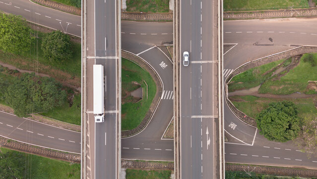 Aerial view of Rodovia Anhanguera highway interchange with a white truck and a car driving on asphalt lanes surrounded by green grass in Araras, Sao Paulo, Brazil.