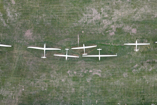 Aerial view of several white gliders parked in a row on a green grassy airfield in the United Kingdom.