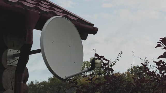 Large satellite dish receiver mounted on a wooden log house. Modern technology for receiving television or internet signal in a rural area