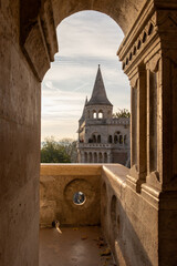 Fisherman's Bastion turret and stone balcony framed by a carved archway in Budapest, Hungary. Scenic architectural view of the iconic fortress during warm morning light. © Bill Lezos