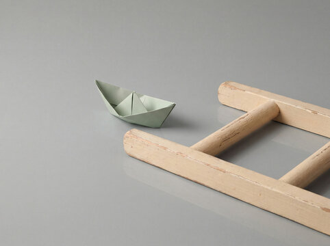 Paper boat beside wooden toy raft on a gray surface