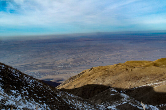 Snow covered mountain slopes overlooking vast valley under cloudy sky