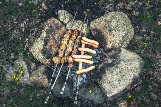 Grilled meat skewers and sausages over charcoal campfire among rocks