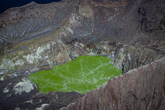 Aerial view of the vibrant green acidic lake inside the volcanic crater of Whakaari White Island, surrounded by rugged rocky slopes in the Bay of Plenty Region, New Zealand.
