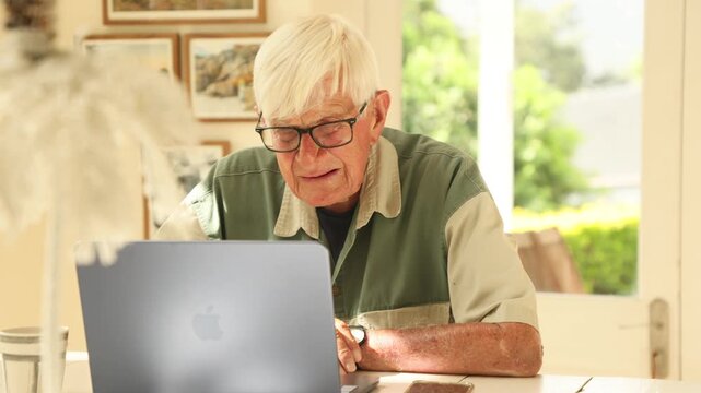 elderly man (90) looking at laptop computer in light filled room