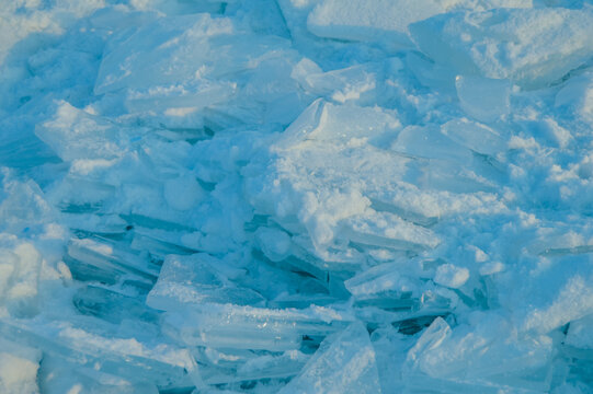 Broken transparent blue ice chunks and snow in winter closeup