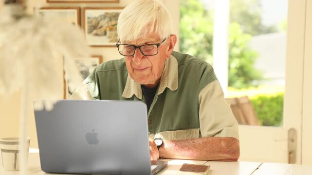 elderly man (90) looking at laptop computer in light filled room